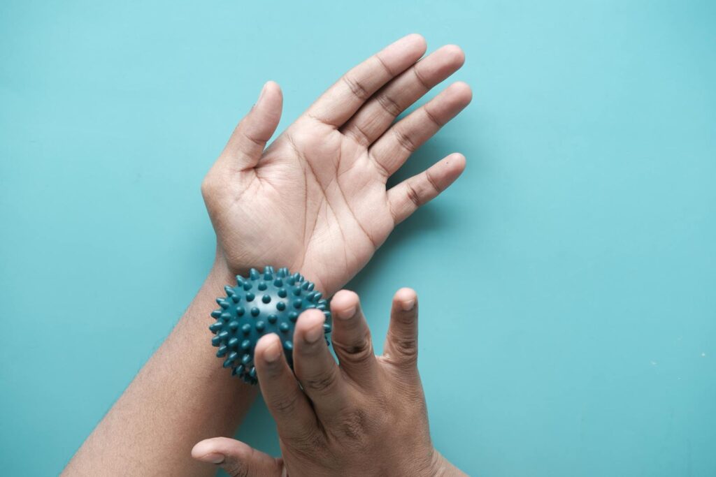 Close-up of hands using a spiky massage ball for therapy against a blue backdrop.