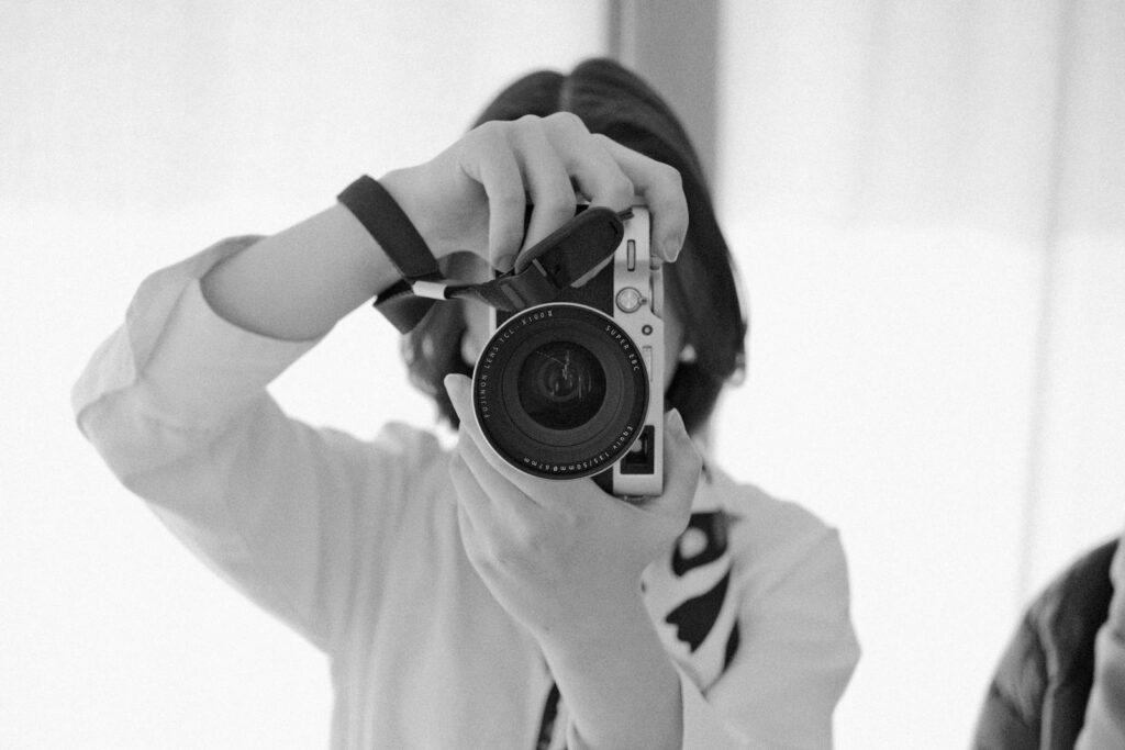 Black and white image of a woman holding a camera aiming at the viewer.