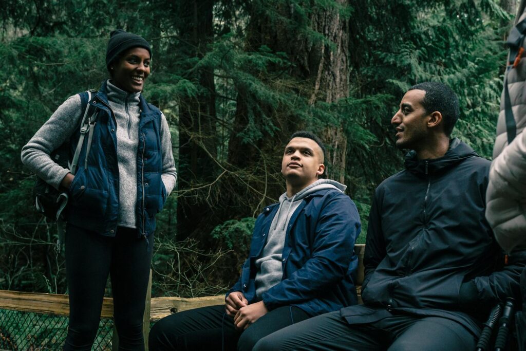 Three friends hiking and relaxing in a lush forest setting, engaging in conversation.