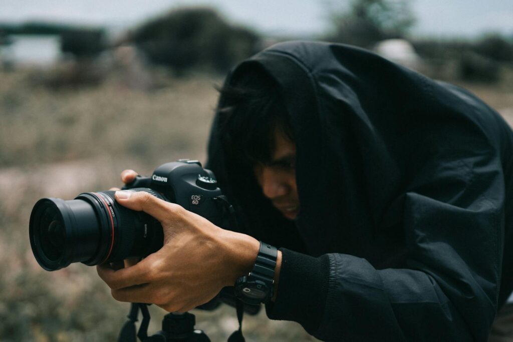 A photographer focused outdoors, capturing moments with a camera, wrapped in a dark coat.