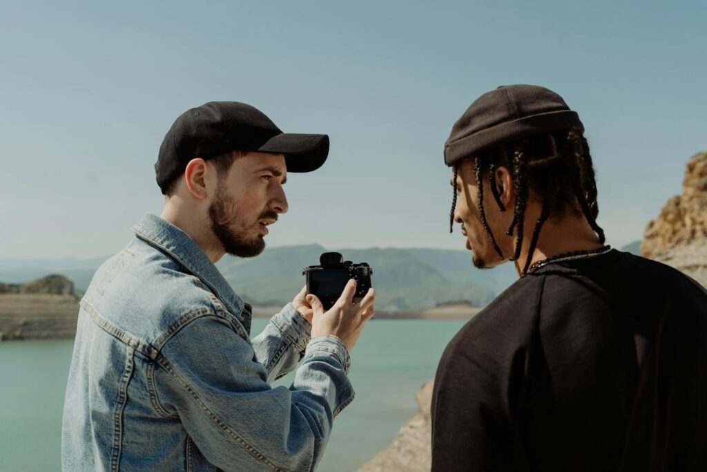 Two men outdoors by a lake discussing photography with a camera in a casual setting.