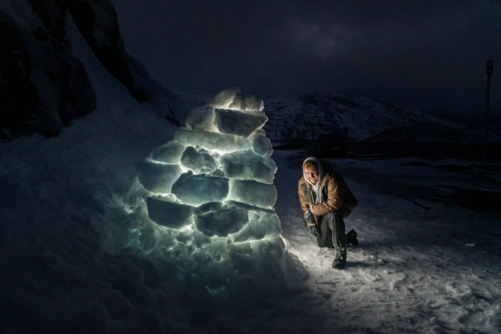 A man kneeling down next to a snow sculpture