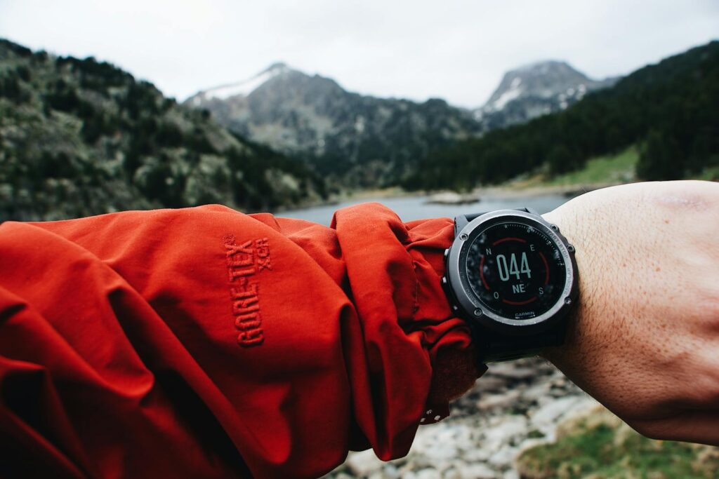 A hiker checks digital watch amid mountainous landscape. Adventure awaits.