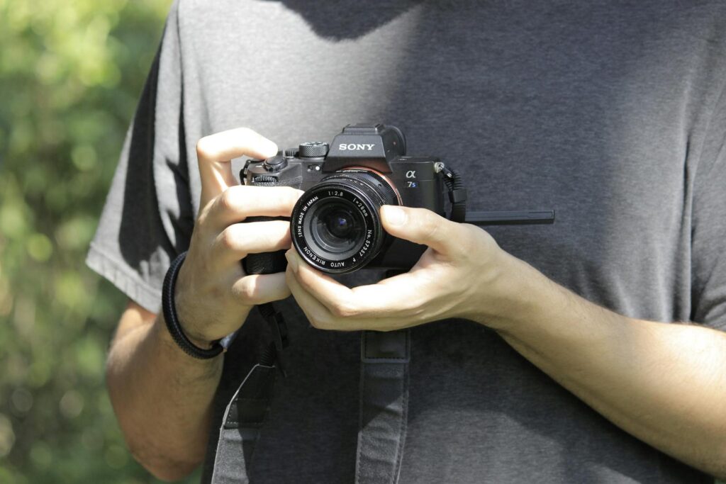 A person holds a camera outdoors, showcasing the equipment with a natural background.
