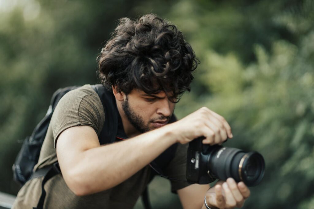 A focused young man with a DSLR camera photographing nature outdoors.