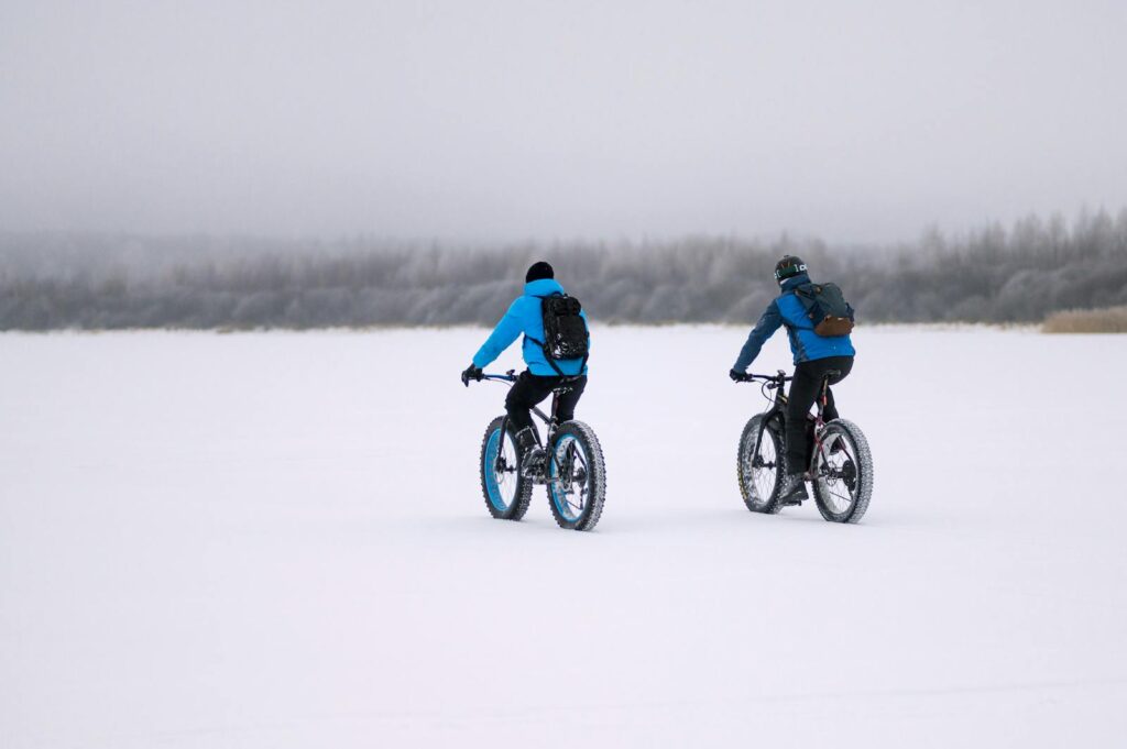Two cyclists riding fat bikes through a snowy landscape, embracing winter sports and adventure.