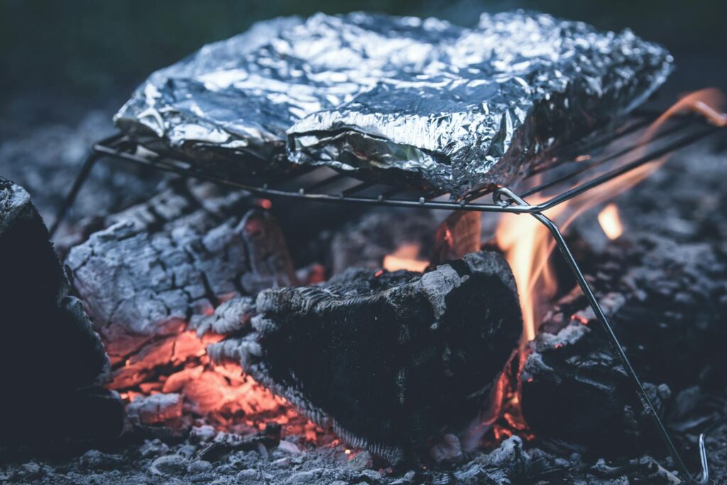 Close-up of foil-wrapped food grilling over an open flame. Perfect for BBQ enthusiasts and outdoor cooking.