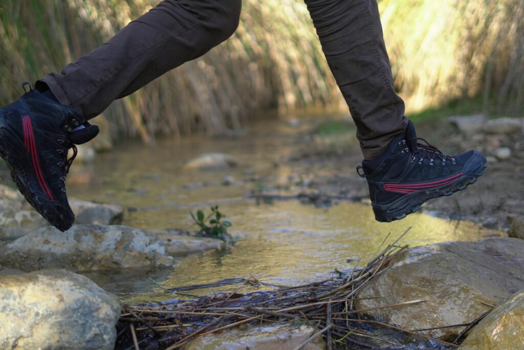 Dynamic close-up of boots leaping over stones in a shallow stream.