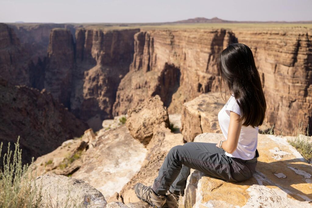 Young woman sits on cliff edge at Grand Canyon, Arizona, taking in breathtaking views.