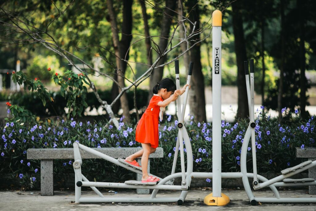 A young girl in a vibrant dress uses an elliptical trainer in a lush park setting.