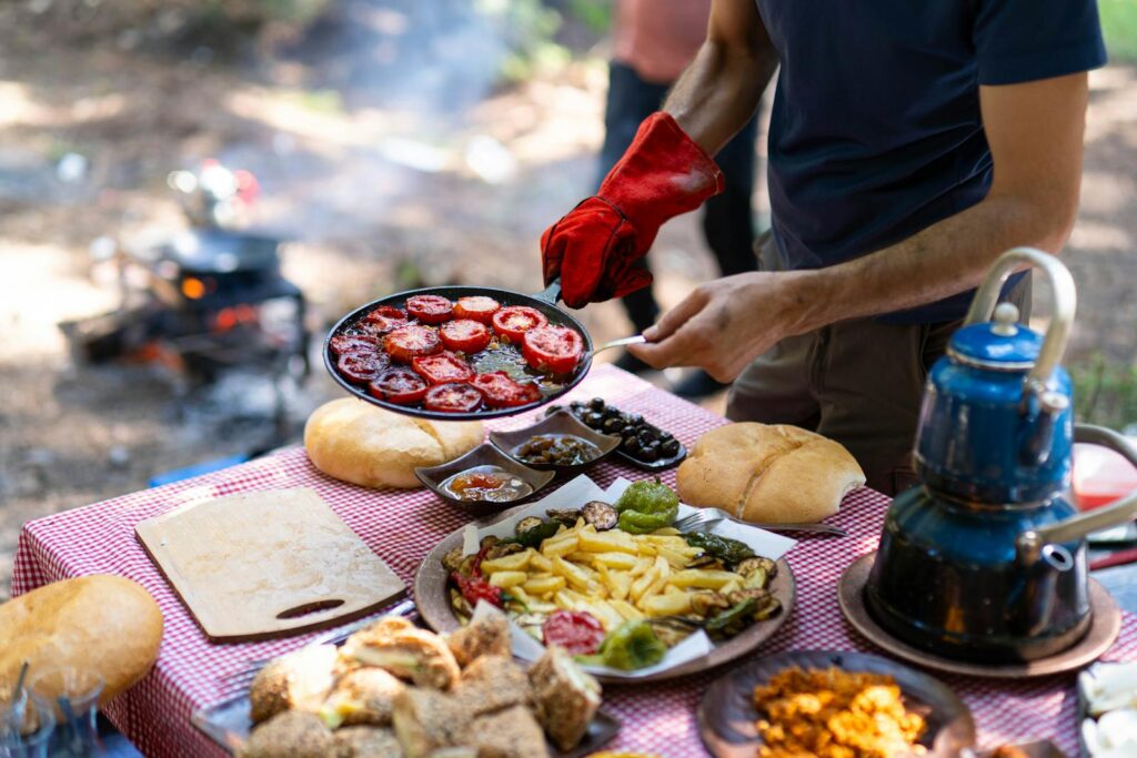 Enjoying an outdoor culinary experience with grilled tomatoes and various side dishes by the campfire.