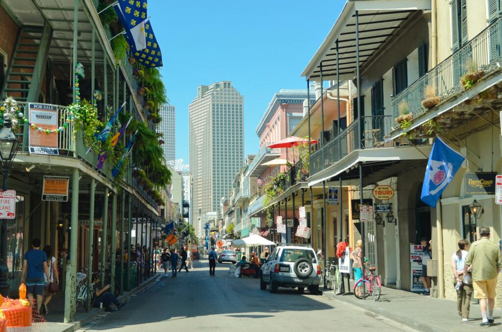 Explore a lively New Orleans street bustling with pedestrians, cars, and iconic architecture under a clear summer sky.