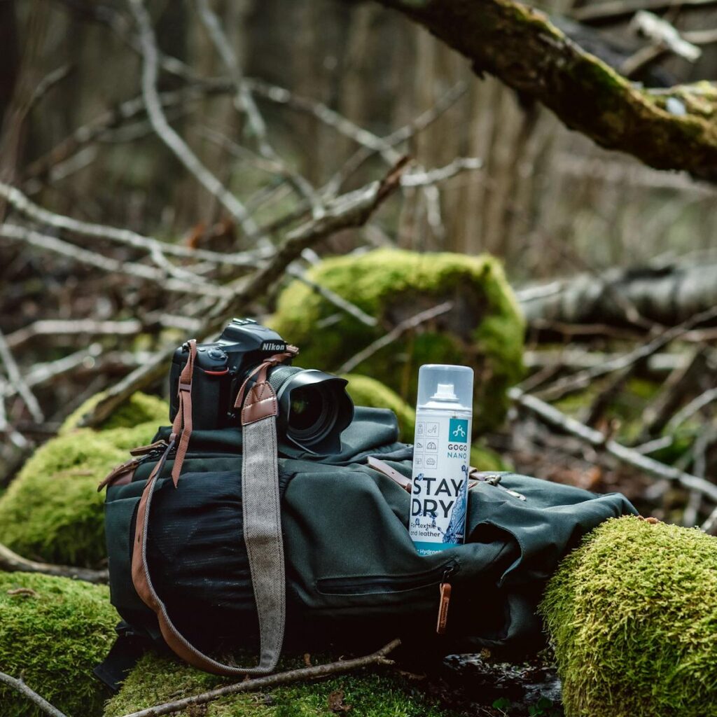 Camera and waterproof spray on a backpack in a mossy forest setting, perfect for outdoor photography enthusiasts.