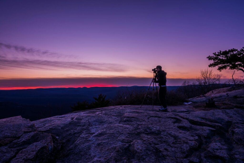 A photographer takes a stunning sunset shot from a rocky mountain peak.