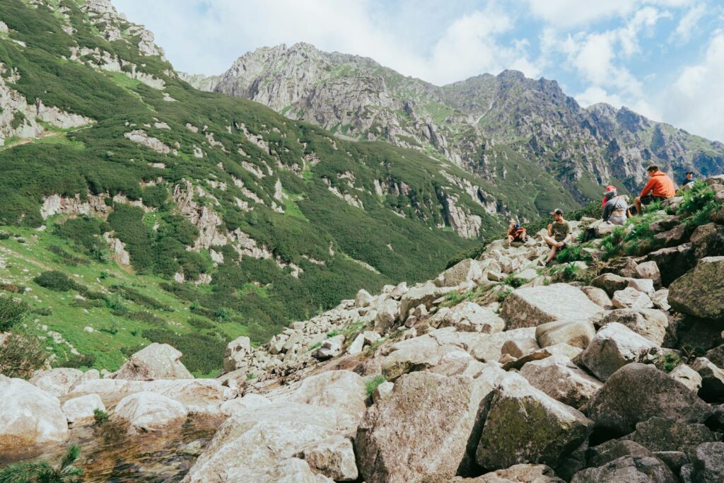 A group of hikers resting on a rocky slope in the picturesque Tatra Mountains under a clear summer sky.