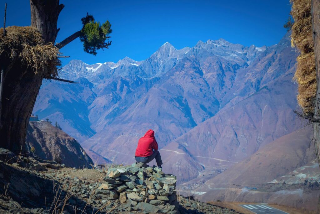 A lone traveler in a red jacket admires the vast mountain range in Juphal, Nepal.