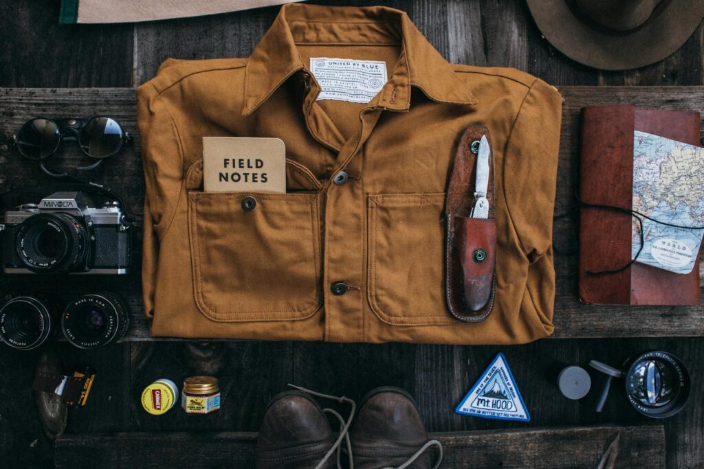 Top view layout of costume of traveler with notepad and knife placed near photo camera and lenses on surface near diary with map
