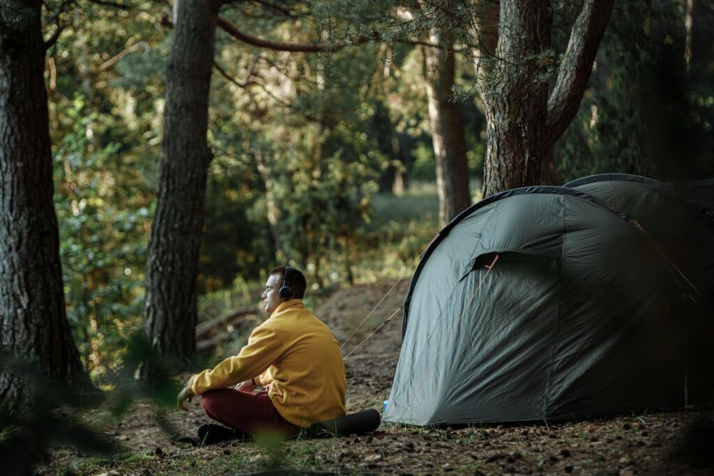 A person enjoying a calm morning by a tent in a forest wearing headphones.