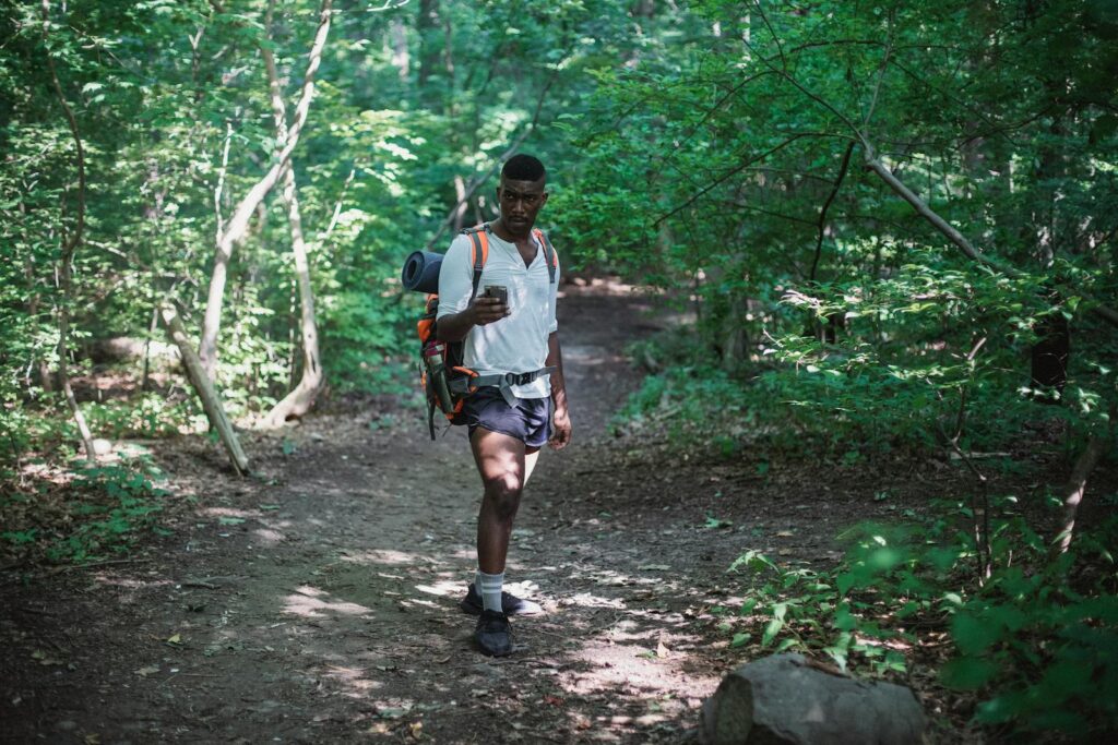 African American hiker exploring a lush green forest trail while using a smartphone for navigation.