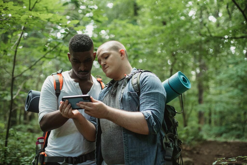 Focused multi ethnic backpackers watching smartphone while finding location in woodland in daytime on blurred background