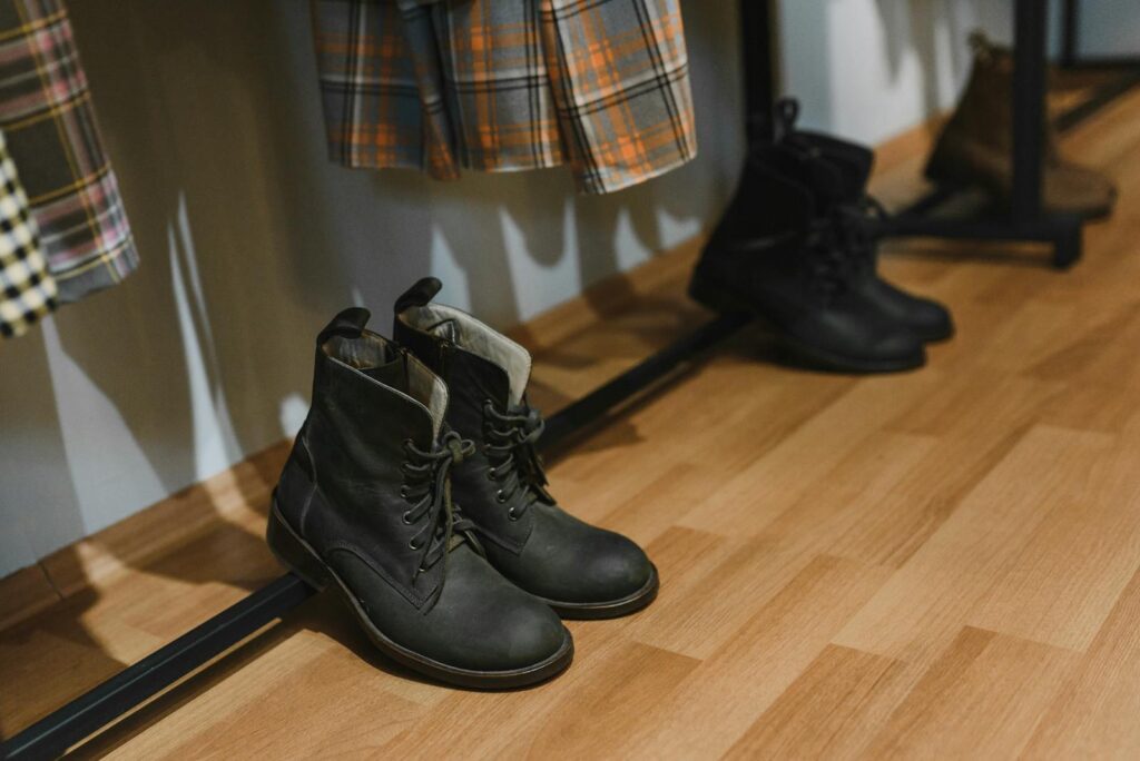 Close-up of black leather boots on a wooden floor beneath colorful plaid clothing.