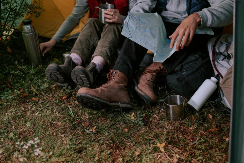 Two people relaxing outdoors, enjoying camping with boots, maps, and drinks.