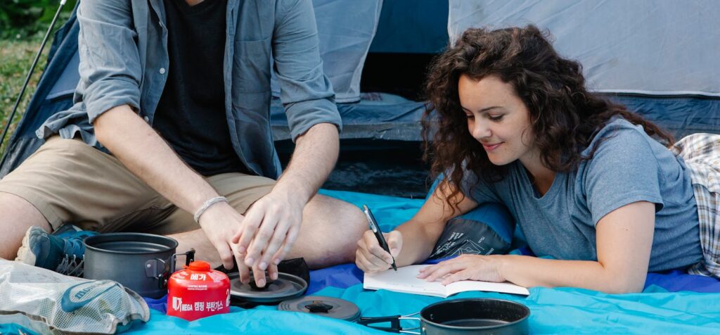 A cheerful couple camping outdoors, writing notes around camping gear in a tent.