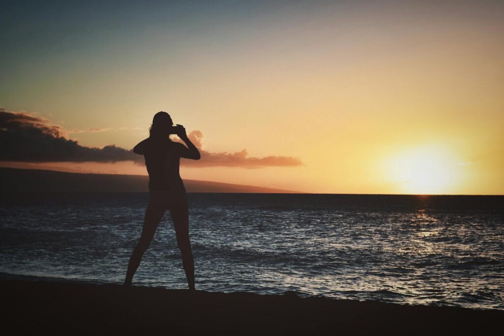 A silhouette of a person against a colorful sunset at the beach, capturing the serene ocean view.
