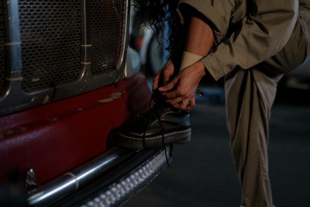 Close-up of a woman in work attire tying her boot on a truck bumper, emphasizing resilience.