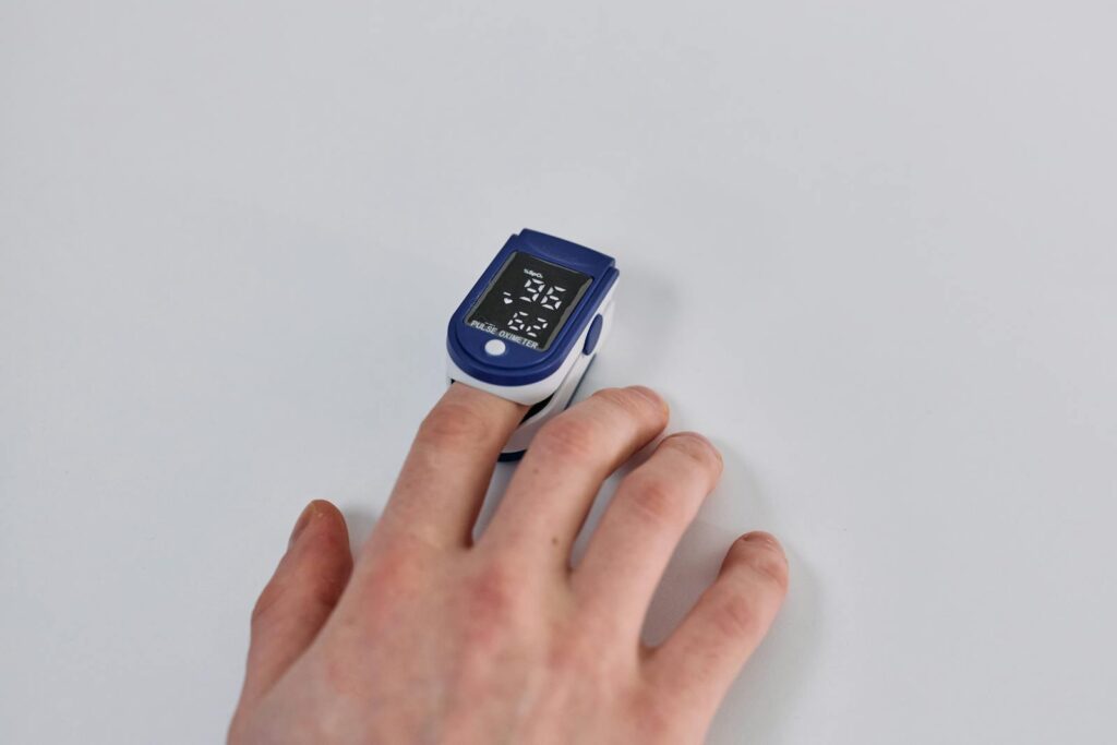 Close-up of a hand using a pulse oximeter to measure oxygen levels on a white background.