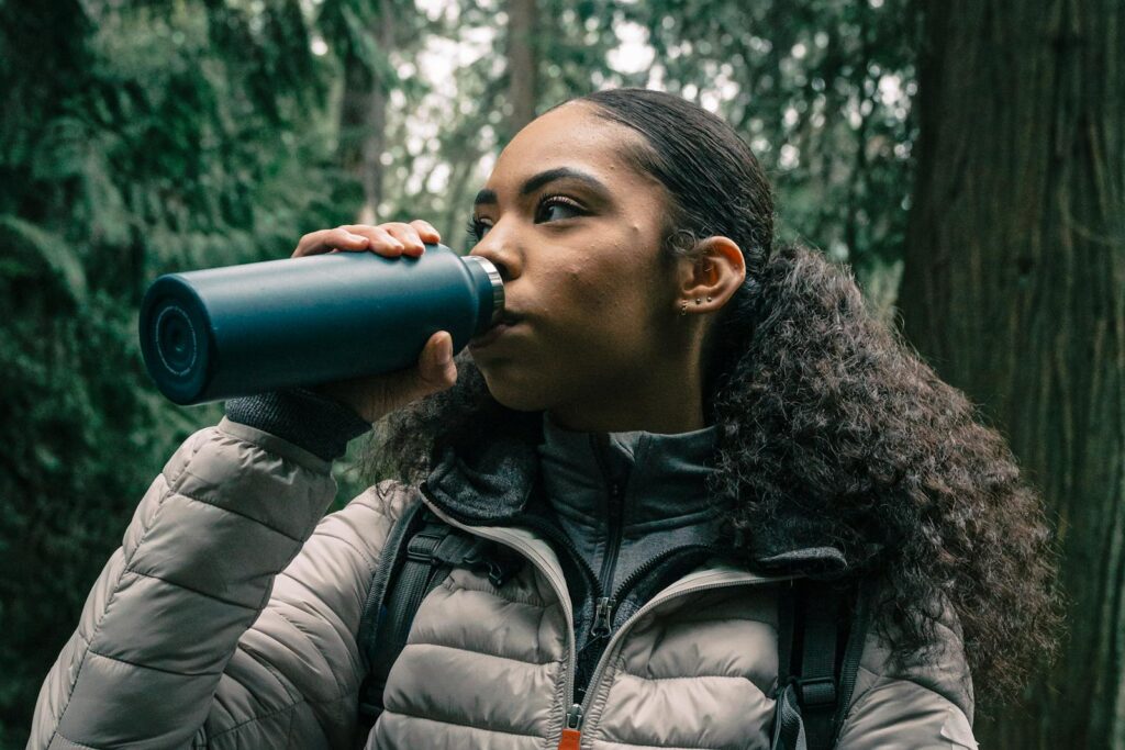 Young woman drinking from water bottle while hiking in a forest.