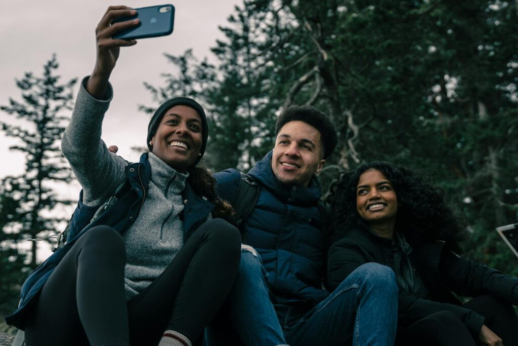 Three friends smiling and taking a selfie while hiking in a forest.