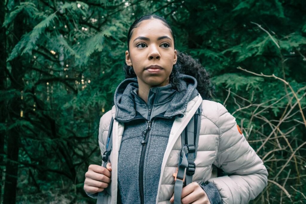 Pensive woman in a bubble jacket hiking through a forest, embracing adventure.