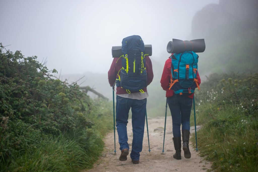 A couple with backpacks and trekking poles hiking through a misty path in Portugal.
