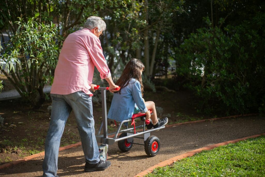 A joyful moment of a grandfather pushing his granddaughter on a garden cart in a sunny park.