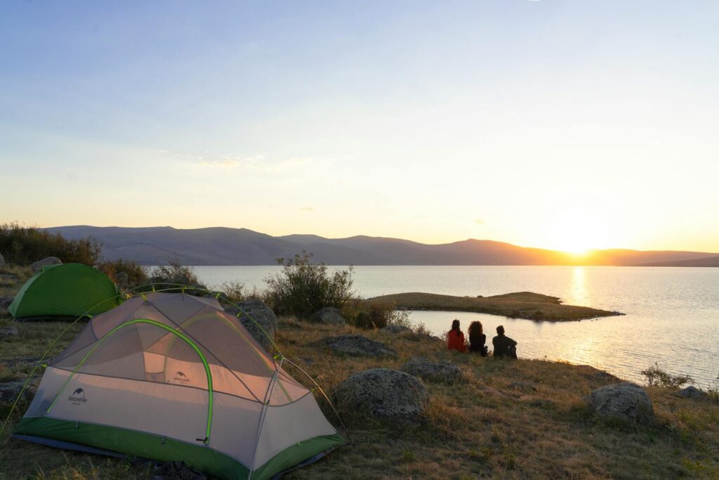 Tranquil lakeside camping scene at sunrise with tents and people in Türkiye.
