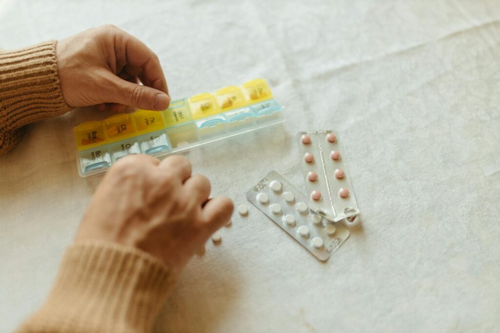 Close-up of hands organizing tablets into a weekly pillbox for daily medication management.