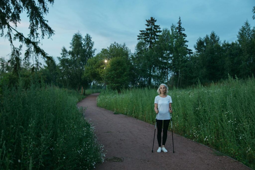 Senior woman exercising with Nordic walking poles in a peaceful green park during daytime.