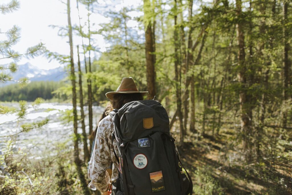 A solo backpacker trekking through a sunlit forest with mountain views.