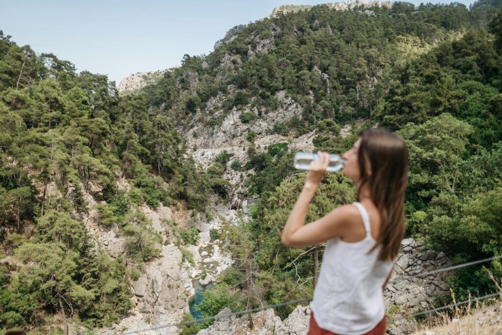 A woman enjoys a refreshing drink while taking in a stunning mountain view.