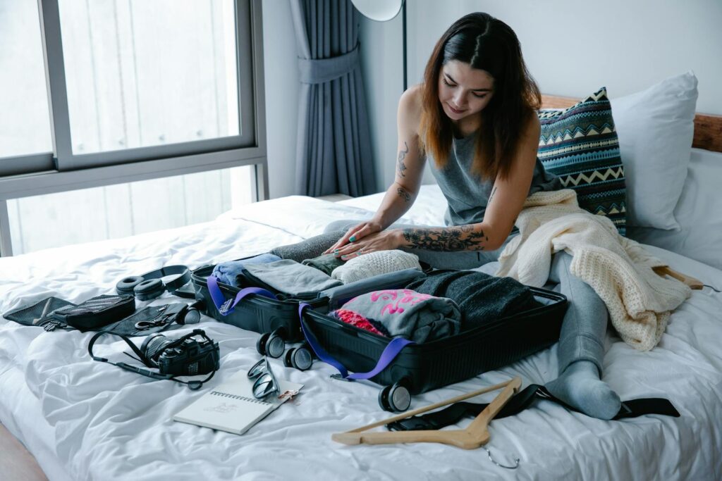 Woman sitting on bed packing suitcase with clothes and travel essentials.