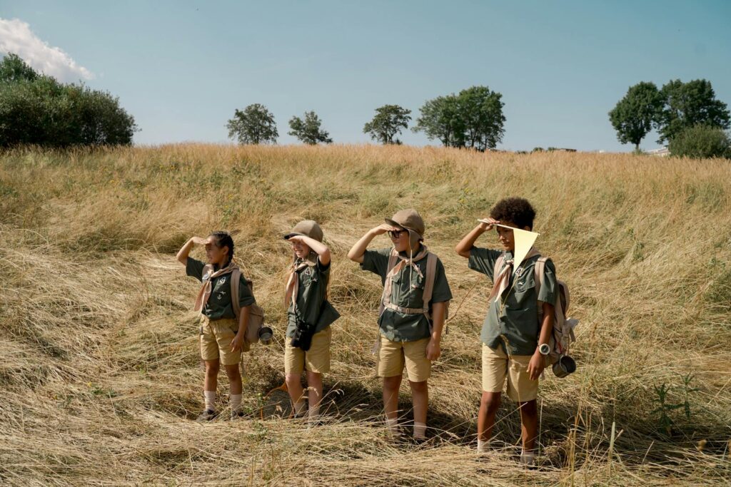 A group of children in scout uniforms exploring a sunny field on a summer day.