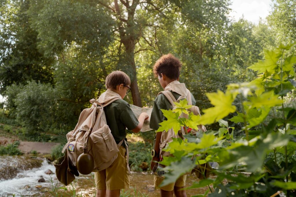 Two young scouts in uniforms exploring a forest with a map by a stream.