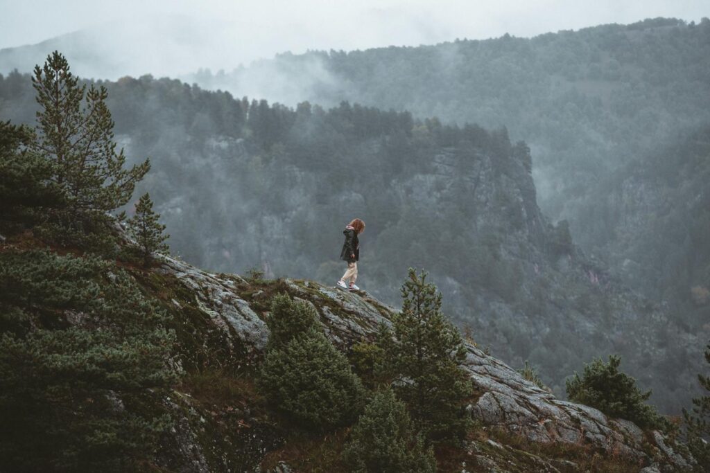 A lone hiker stands on a misty mountain slope, surrounded by fog and trees, capturing the essence of adventure.