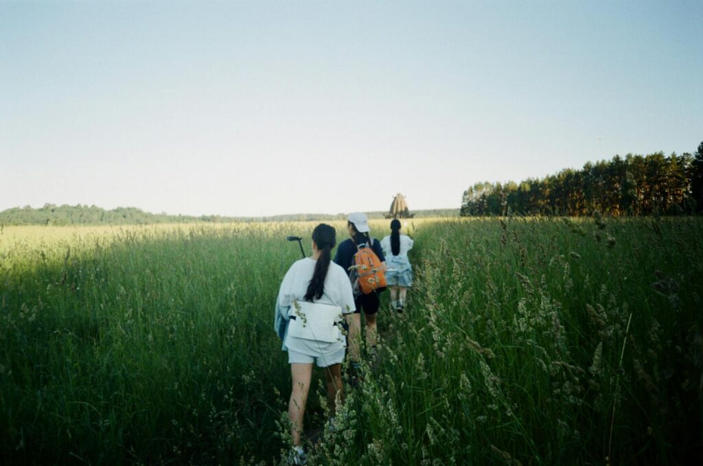 A group of women hiking through tall grass in the countryside on a sunny day.