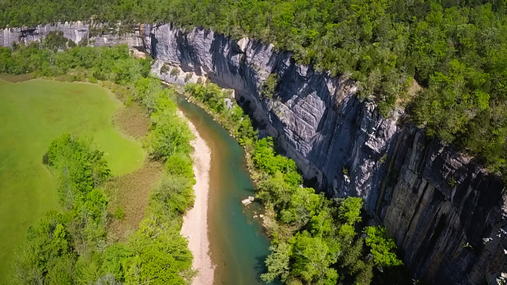 Aerial view of a winding river bordered by lush greenery and steep rocky cliffs, showcasing a serene natural landscape.