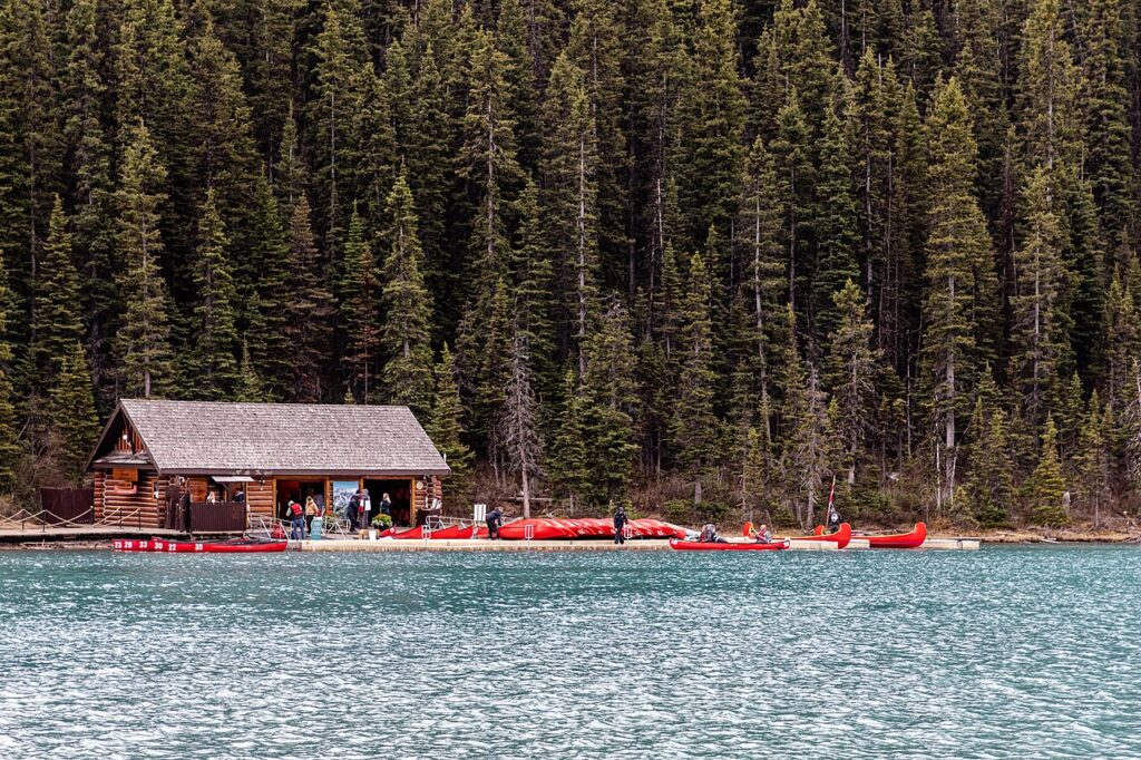 A cozy wooden cabin by a serene lake, with kayaks docked and people preparing for water activities against a backdrop of tall pine trees.