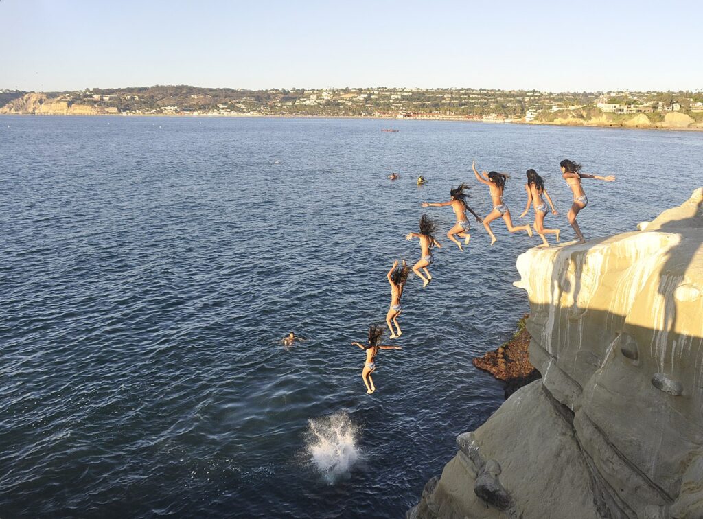 A sequence of girls in bikinis jumping off a cliff into the ocean, capturing the thrill and excitement of summer fun.