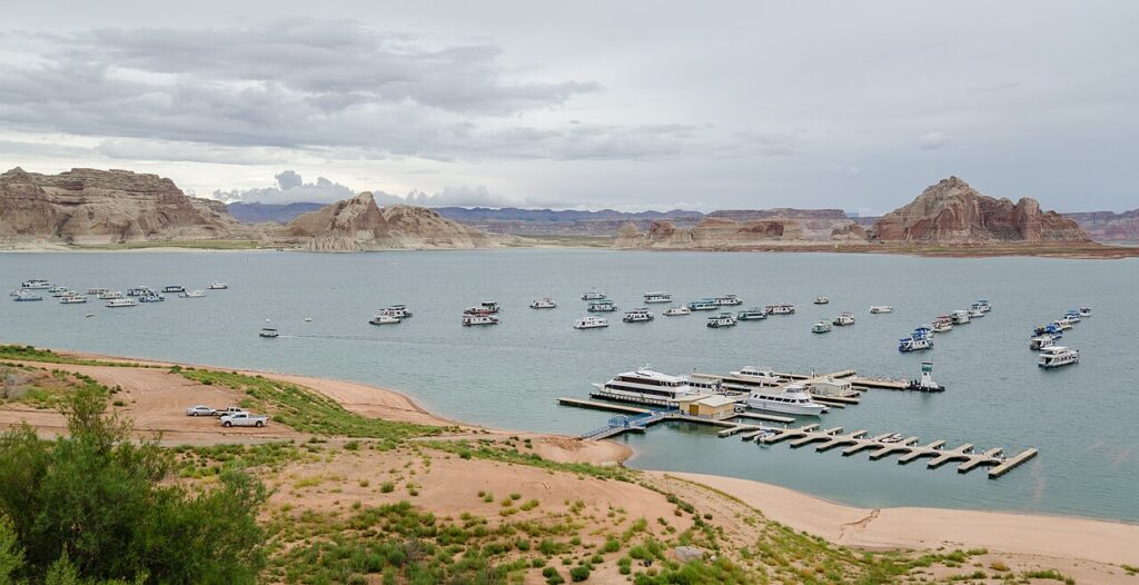 A picturesque lake scene featuring numerous boats moored near a dock, with rocky cliffs and cloudy skies in the background.