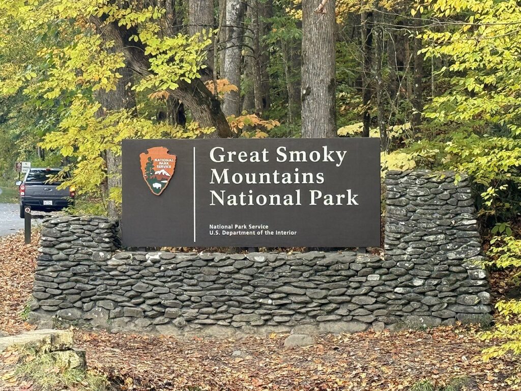 Welcome sign for Great Smoky Mountains National Park surrounded by colorful autumn foliage and stone landscaping.